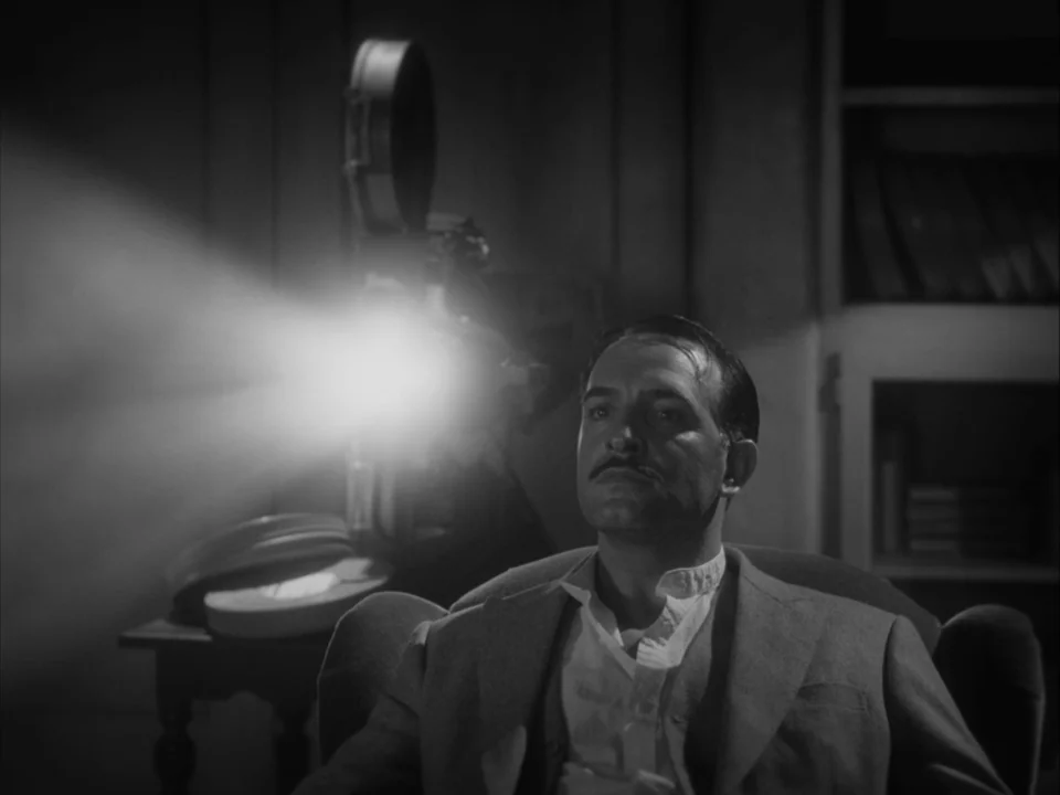 The Artist (2011) movie still: medium — A dark room contains a vintage film projector casting a bright cone of light. A man with a mustache sits in…