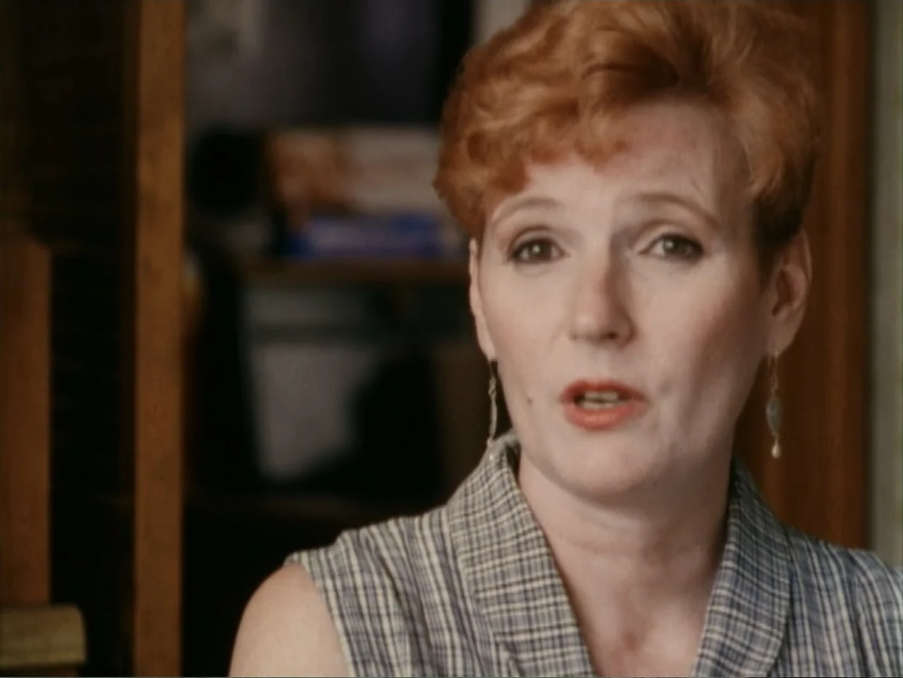 5 American Handguns - 5 American Kids (1995) movie still: closeup — A woman stands indoors against a blurred residential background with wooden door…