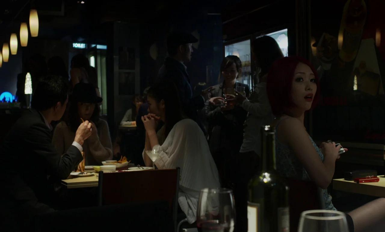 Like Someone In Love (2012) movie still: medium — A dimly lit establishment features patrons sitting at tables amidst soft ambient wall lighting.…