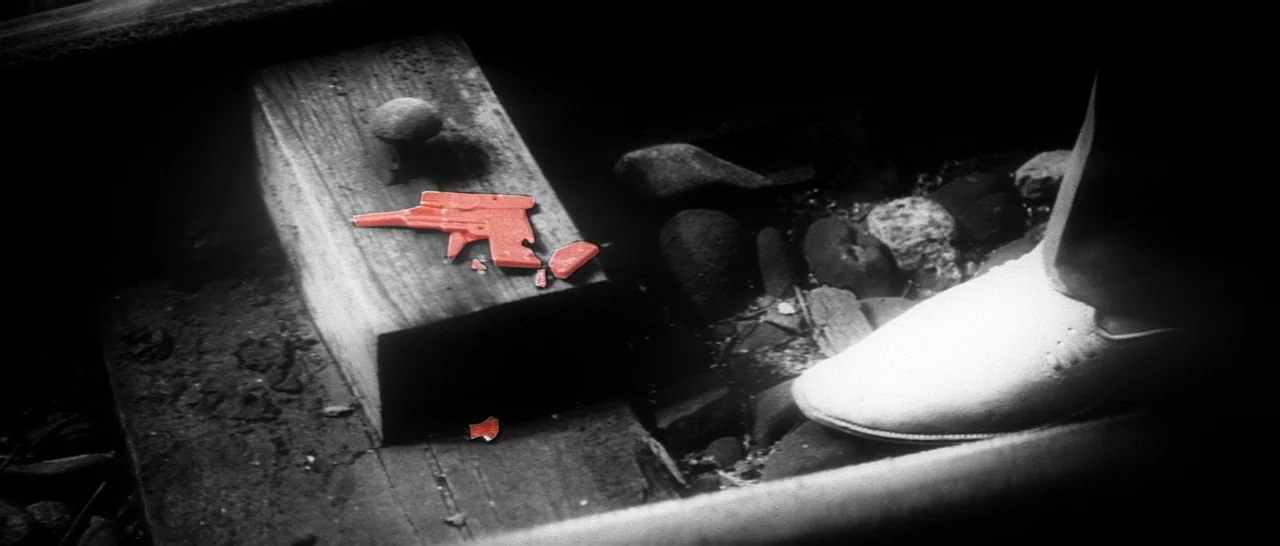 Tokyo Drifter (1966) movie still: closeup — A broken red plastic toy gun rests on a weathered wooden railroad tie. A white shoe stands on the gravel…
