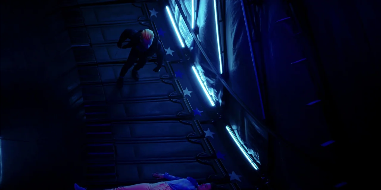 Totally Killer (2023) movie still: wide — A dark, angled corridor features repeating blue star wall decorations and parallel neon light strips. A…