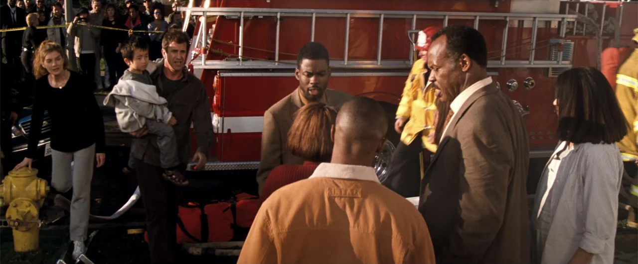 Lethal Weapon 4 (1998) movie still: medium — A group of people stands outside near a large red fire truck with a ladder. A man holds a small boy…