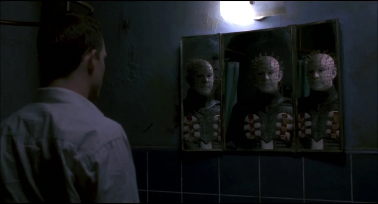 Hellraiser: Hellseeker (2002) movie still: medium — A dimly lit room with blue tiled walls and a small wall-mounted vanity mirror. A man faces the…