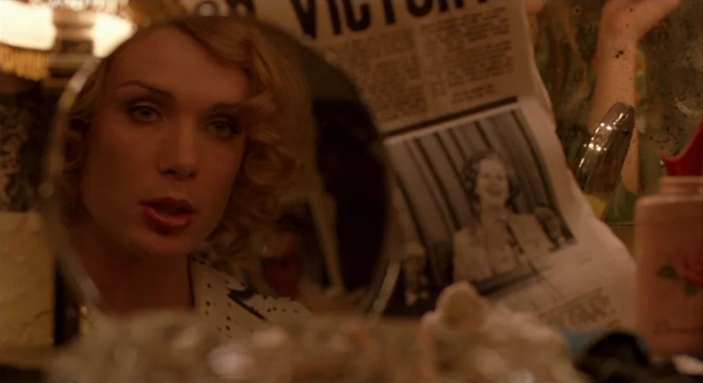 Breakfast On Pluto (2005) movie still: closeup — A dimly lit room features a cluttered vanity with a newspaper clipping visible. A person looks…