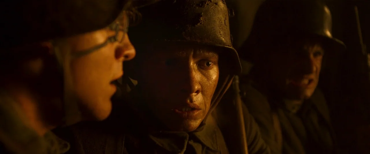 All Quiet on the Western Front (2022) movie still: medium — Three soldiers sit closely together in a dark, confined subterranean dugout. The men…