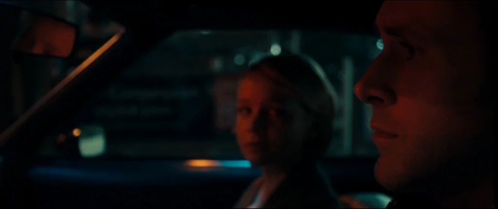 Drive (2011) movie still: medium — The interior of a vehicle at night with blurred lights passing by the windows. A man and woman sit side-by-side…