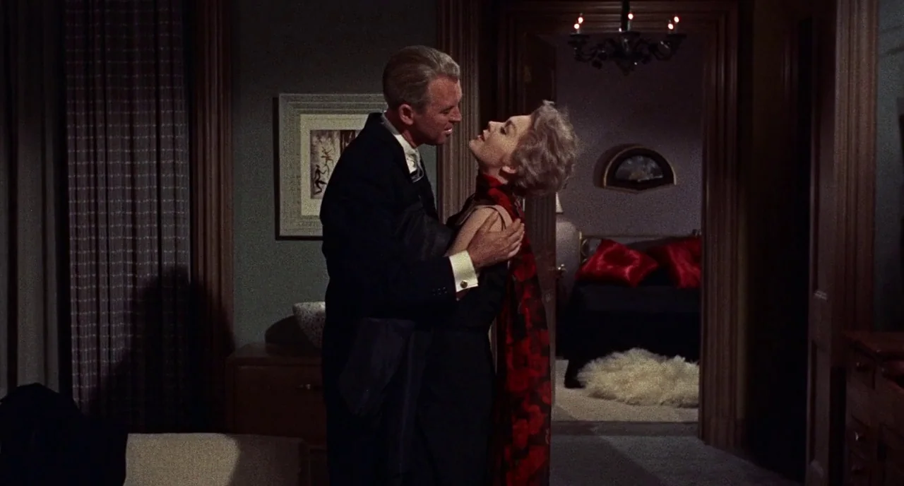 Bell Book and Candle (1958) movie still: medium — A dimly lit room with framed art and dark wood trim leads into another space. A man and a woman…