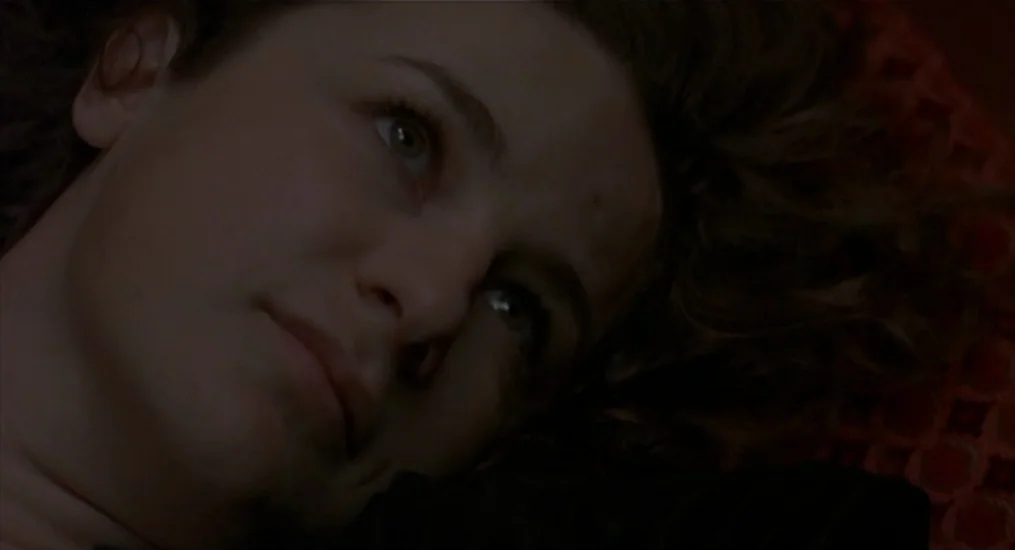 Vendredi Soir (2002) movie still: closeup — A close-up view of a person lying on a patterned red fabric surface. The subject is angled with their…