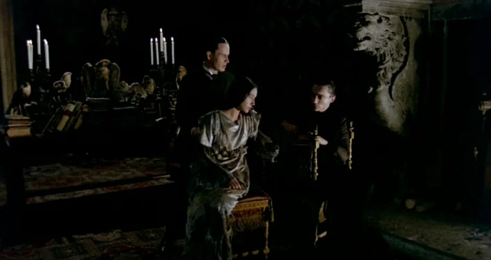 Blood For Dracula (1974) movie still: medium — A dimly lit room features a large stone lion carving and ornate wooden furniture. Two men and one…