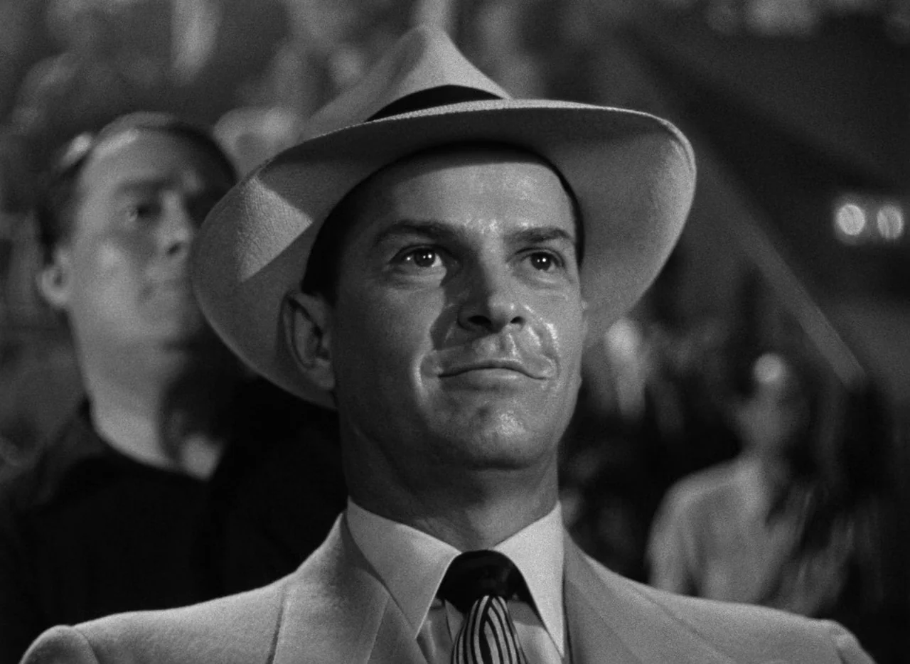 The Set-Up (1949) movie still: closeup — A man wearing a formal suit and felt hat stands at a public event. He gazes forward with a calm, subtle…