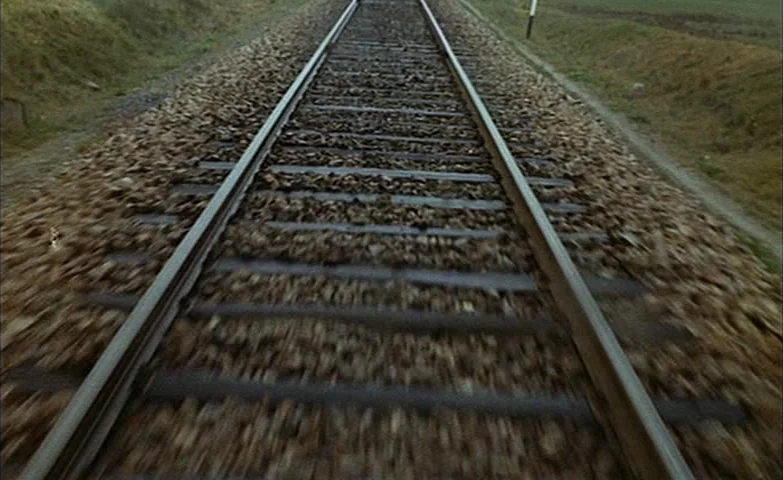 Spirit Of The Beehive (1973) movie still: establishing — A rural railway track stretches toward the horizon through a grassy landscape. Gravel…