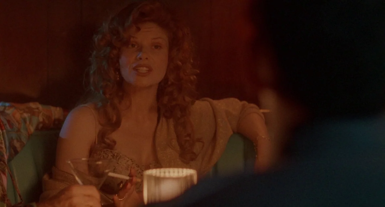 Touch (1997) movie still: medium — A dimly lit restaurant interior features wood-paneled walls and a turquoise booth seat. A woman sits across from…