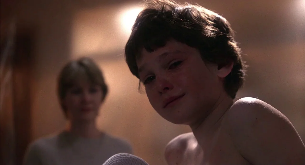E.T. The Extra-Terrestrial (1982) movie still: closeup — A dimly lit room provides a background for two individuals. A tearful child in the…