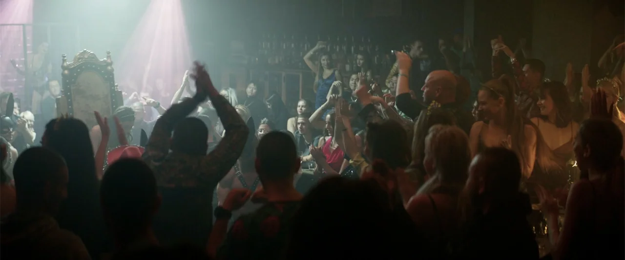 Marked Men: Rule + Shaw (2025) movie still: wide — A crowded dimly lit nightclub interior filled with people and a prominent stage throne. The crowd…