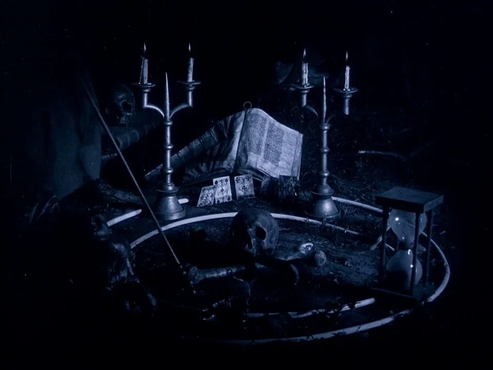 Häxan (1922) movie still: medium — A dark, circular chalk boundary contains a human skull, playing cards, and bones. Two iron candelabras flank an…