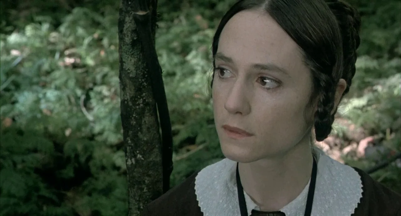 The Piano (1993) movie still: closeup — A dense woodland area with green ferns and a dark tree trunk visible. A woman with dark hair in a…