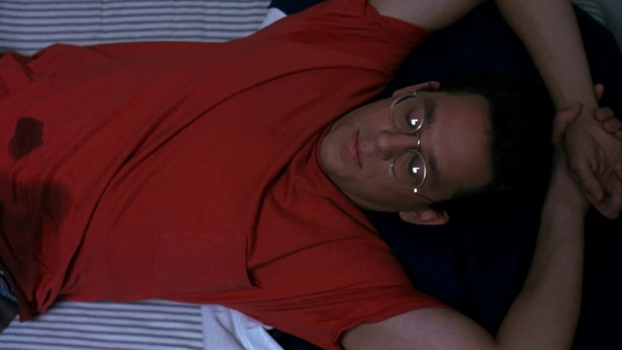 Jason Goes To Hell (1993) movie still: medium — A man lies on a striped sheet with his arms raised behind his head. He wears a plain red pocket…