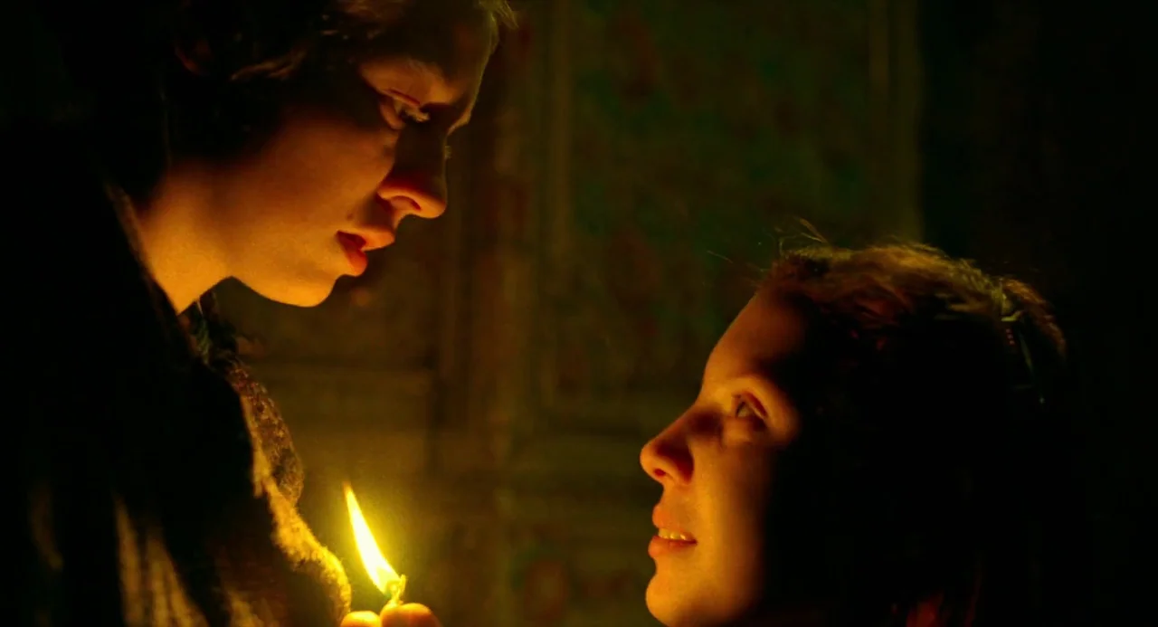 Beanpole (2019) movie still: closeup — A dim room is illuminated only by the flicker of a single small candle. Two women stand face-to-face in the…