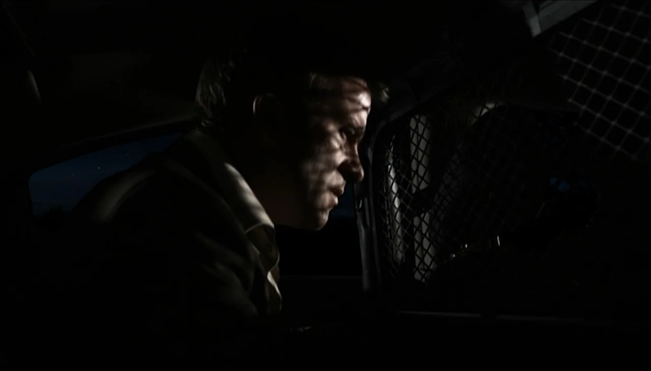 Dark Country (2009) movie still: closeup — A dark vehicle interior features a metallic safety screen between the front and back. A man sits in the…