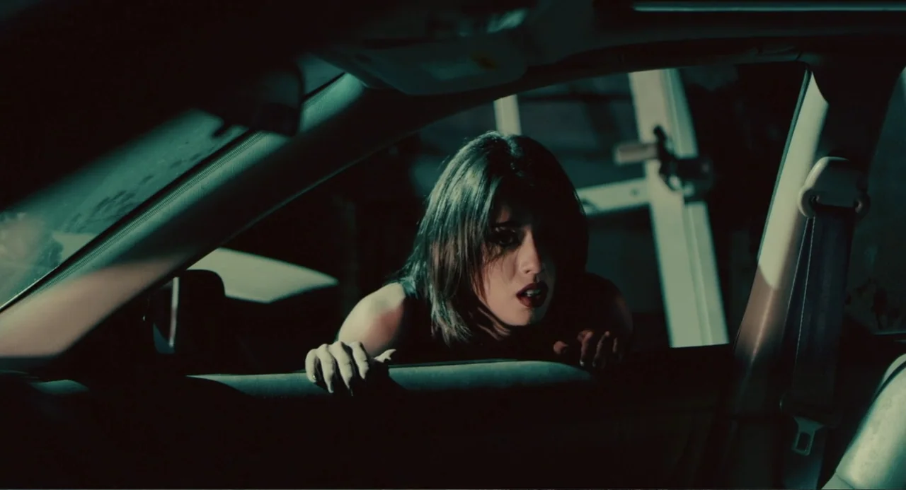 Terrifier (2018) movie still: medium — A dark car interior at night seen through the open driver side window. A young woman with dark hair leans…