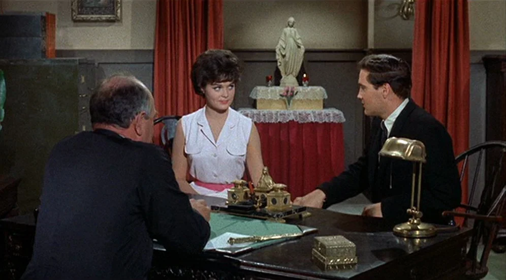 Kid Galahad (1962) movie still: medium — A wood-paneled office contains a large desk and a religious statue on a pedestal. Three people sit around…