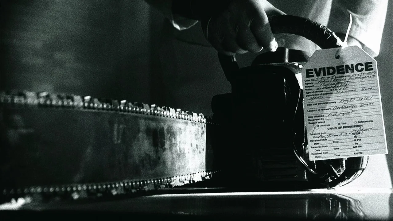 The Texas Chainsaw Massacre (2003) movie still: closeup — A dark environment holds a chainsaw resting on a surface. A white evidence tag is attached…
