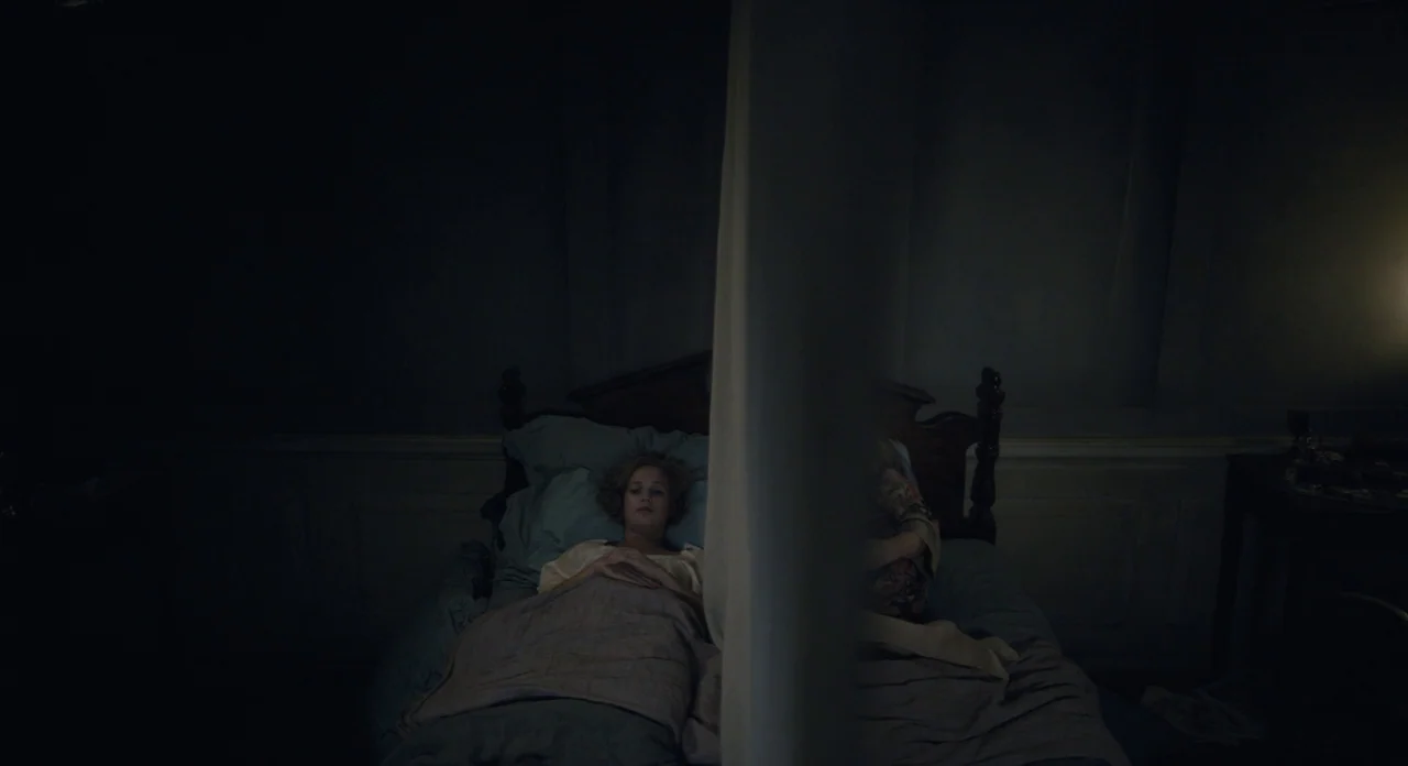 The Danish Girl (2015) movie still: medium — A dark bedroom with two people lying in a bed separated by a vertical curtain. The room is dimly lit…