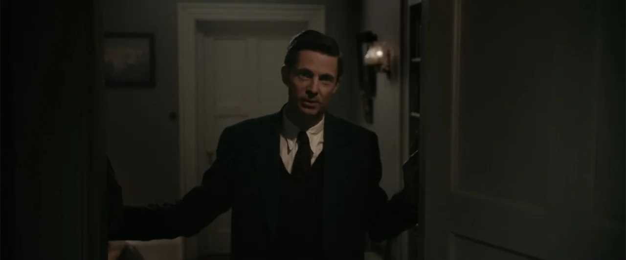 Freud's Last Session (2023) movie still: medium — A dimly lit interior hallway with a dark door frame. A man in a suit stands in the threshold…