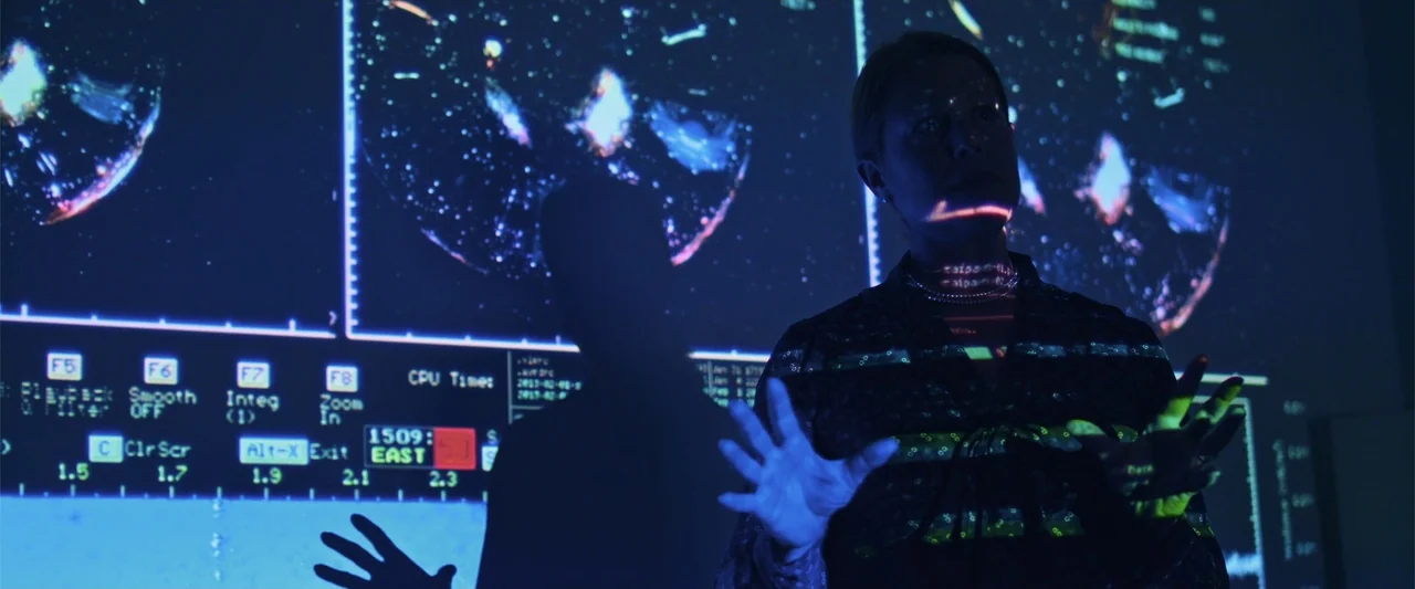 Beyond the Universe (2022) movie still: medium — A dark interior space features a large projected screen displaying technical data and star maps. A…
