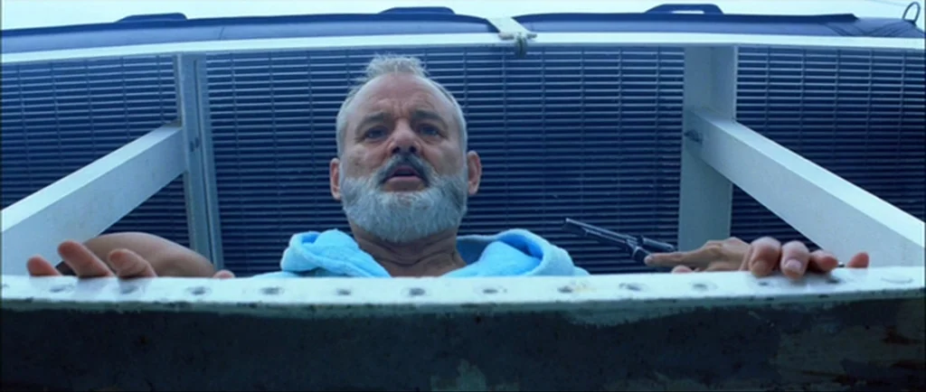 The Life Aquatic With Steve Zissou (2004) movie still: medium — A man looks over a boat railing with a metallic grate backdrop. He grips a handgun…