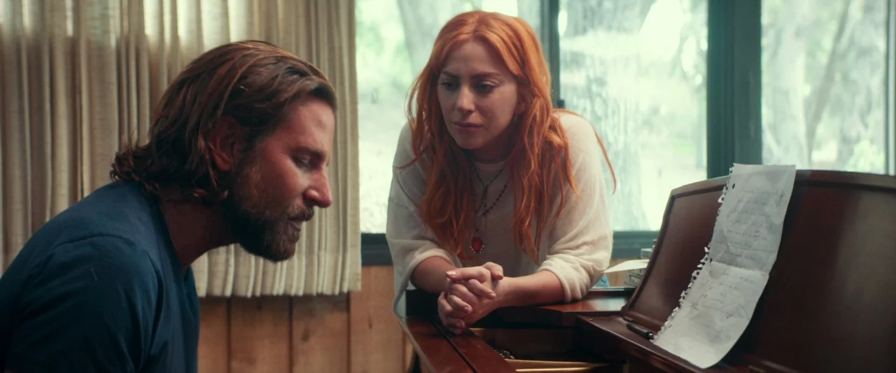 A Star Is Born (2018) movie still: medium — A paneled wall room contains a piano by a large window overlooking trees. A man with a beard sits at the…