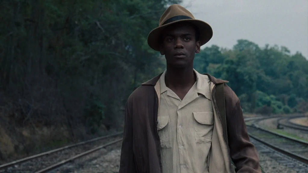 Honeydripper (2007) movie still: medium — A man walks along double train tracks running through a dense, tree-lined landscape. The sky is overcast…