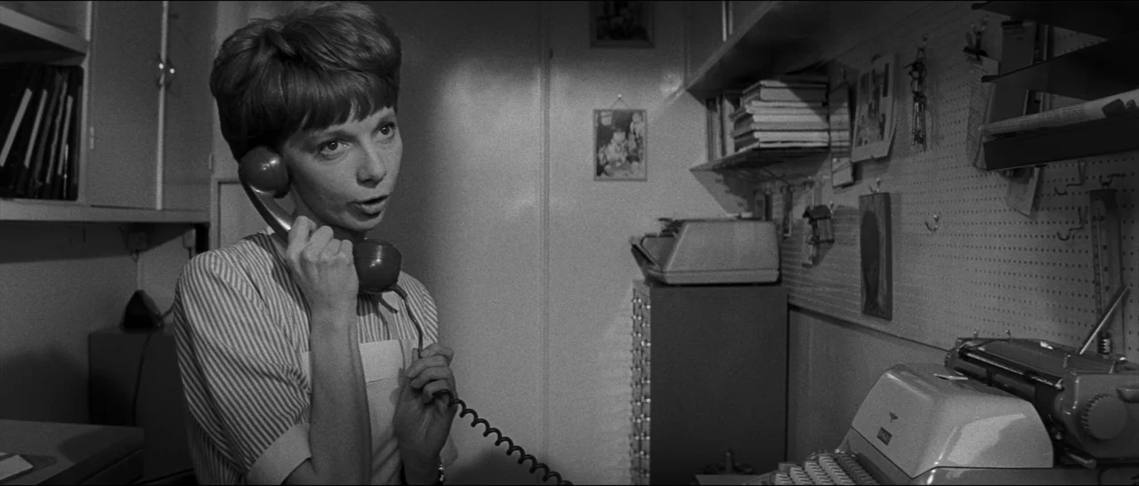 Bunny Lake Is Missing (1965) movie still: medium — A cramped office workspace features a pegboard wall filled with small framed photographs. A young…