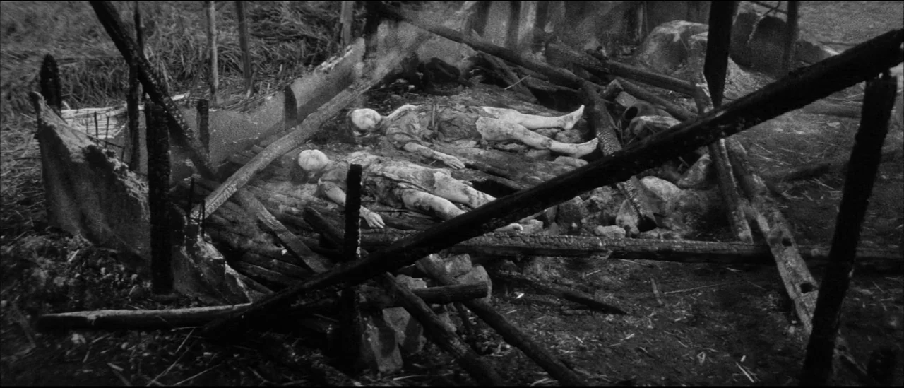 Kuroneko (1968) movie still: wide — A scorched site filled with charred timber debris and broken structural supports. Two motionless figures lie…