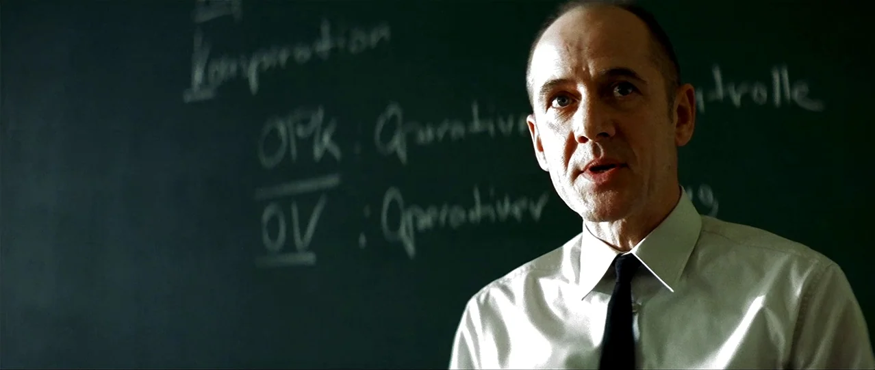 The Lives of Others (2006) movie still: medium — A man stands in front of a green chalkboard containing handwritten German terminology. He is…