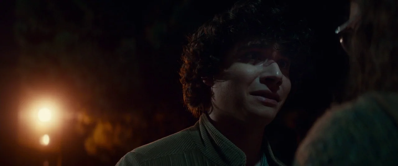 Scary Stories to Tell in the Dark (2019) movie still: closeup — A dark outdoor space at night with only a streetlamp illuminating the subjects. A…