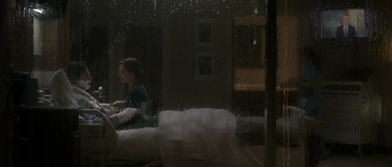 Doctor Strange (2016) movie still: medium — A dimly lit hospital room with medical equipment and a view through a rain-streaked window. A woman sits…