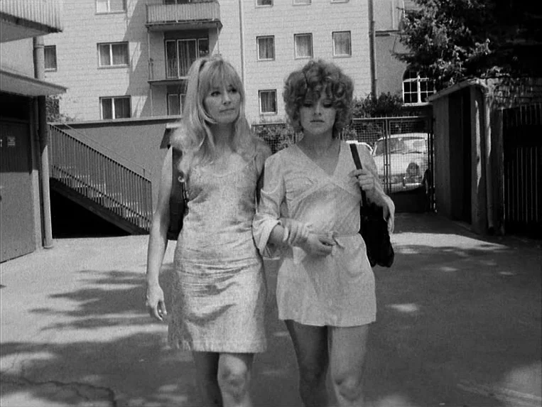 Katzelmacher (1969) movie still: fullbody — An paved courtyard sits before a multi-story residential apartment block with multiple balconies. Two…