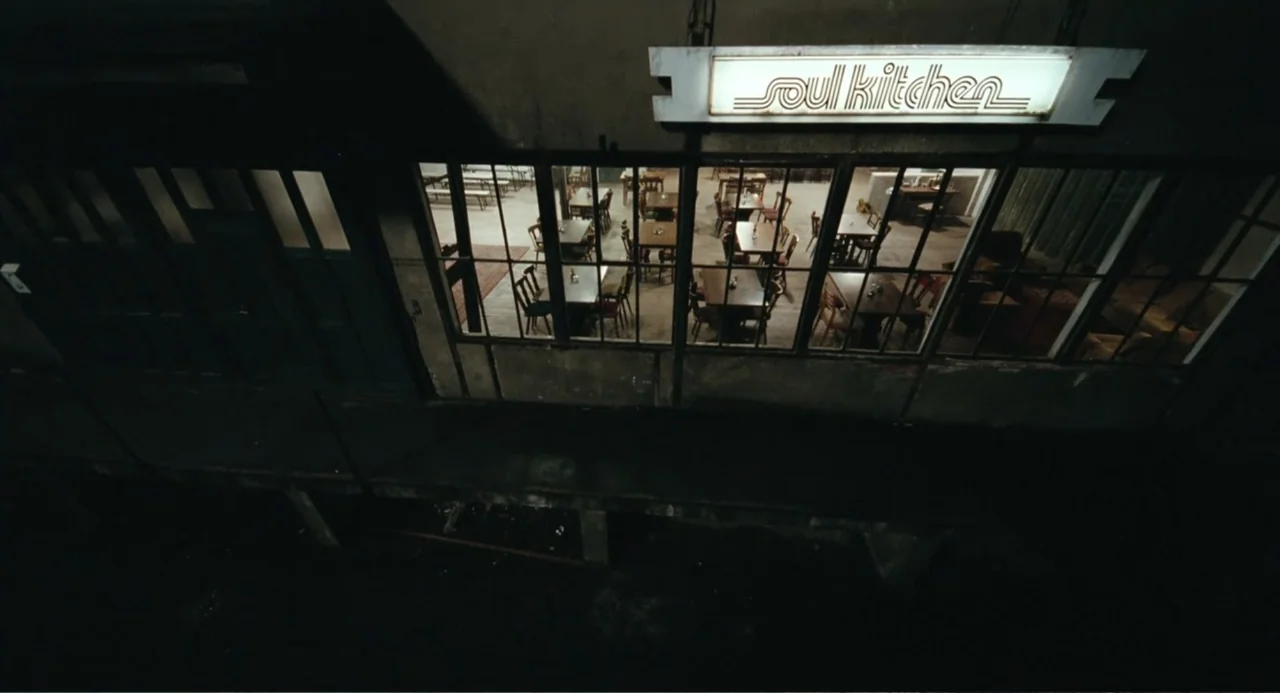 Soul Kitchen (2009) movie still: establishing — A dark street view looks down at a restaurant facade at night. The illuminated soul kitchen sign…