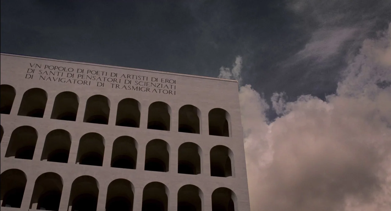 Pasolini (2014) movie still: establishing — The Palazzo della Civiltà Italiana exhibits a repeating pattern of white stone arches. Latin text is…