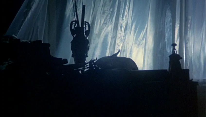 Almanac of Fall (1984) movie still: A dark, moody interior shot focusing on a desktop cluttered with objects, all cast into deep silhouette by a…