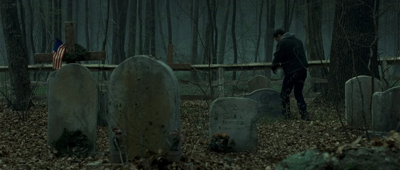 Blood Creek (2009) movie still: wide — An overgrown cemetery with aged stone monuments sits within a dense, leafless forest. A man wearing a dark…