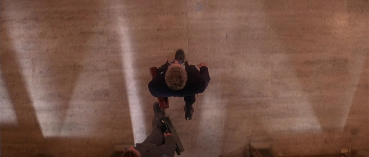 Die Hard with a Vengeance (1995) movie still: wide — A wide view of a beige tiled hallway with rectangular floor panels. Two men in suits carry…