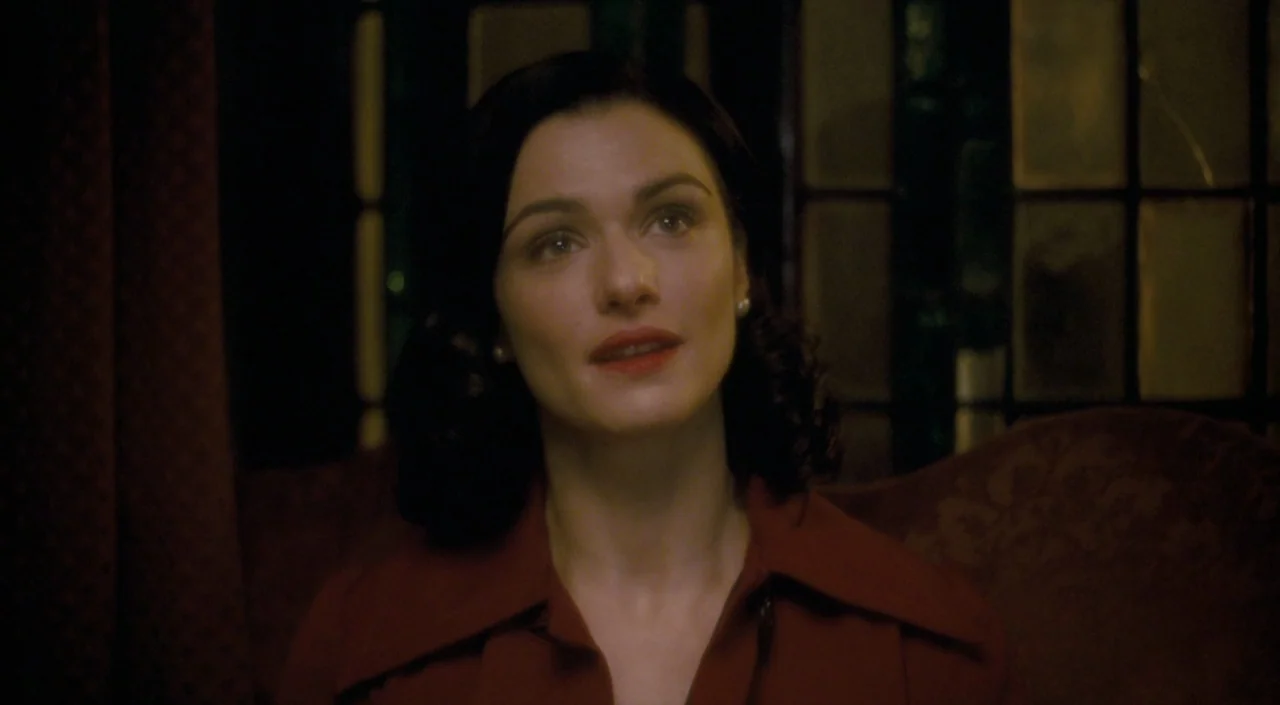 The Deep Blue Sea (2011) movie still: closeup — A dimly lit interior space features a dark window grid in the background. A woman sits in the…