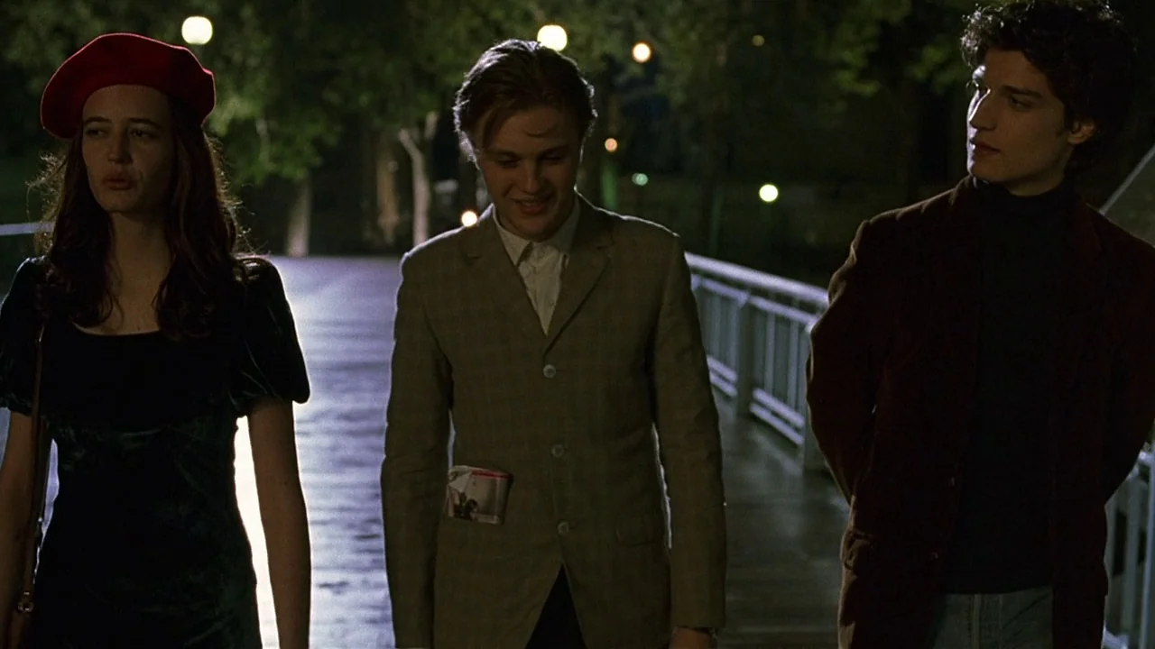 The Dreamers (2003) movie still: medium — A dark outdoor pedestrian bridge at night illuminated by distant circular streetlamps. Three young adults…