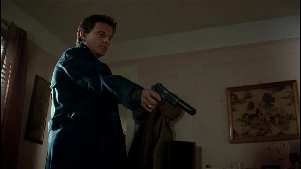 Goodfellas (1990) movie still: medium — An interior room with plain walls, a framed landscape painting, and dark window curtains. A man in a dark…