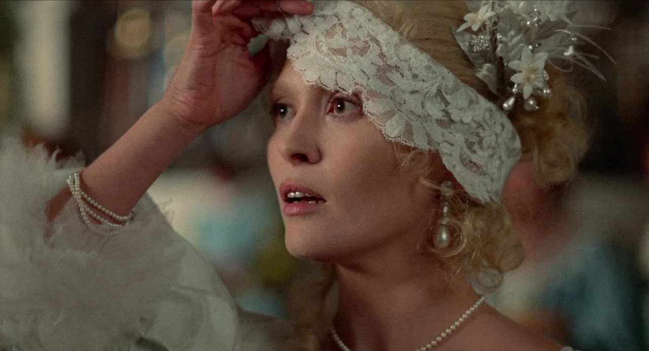 The Three Musketeers (1973) movie still: closeup — A high-society ballroom interior filled with softly blurred guests and warm light. A young woman…