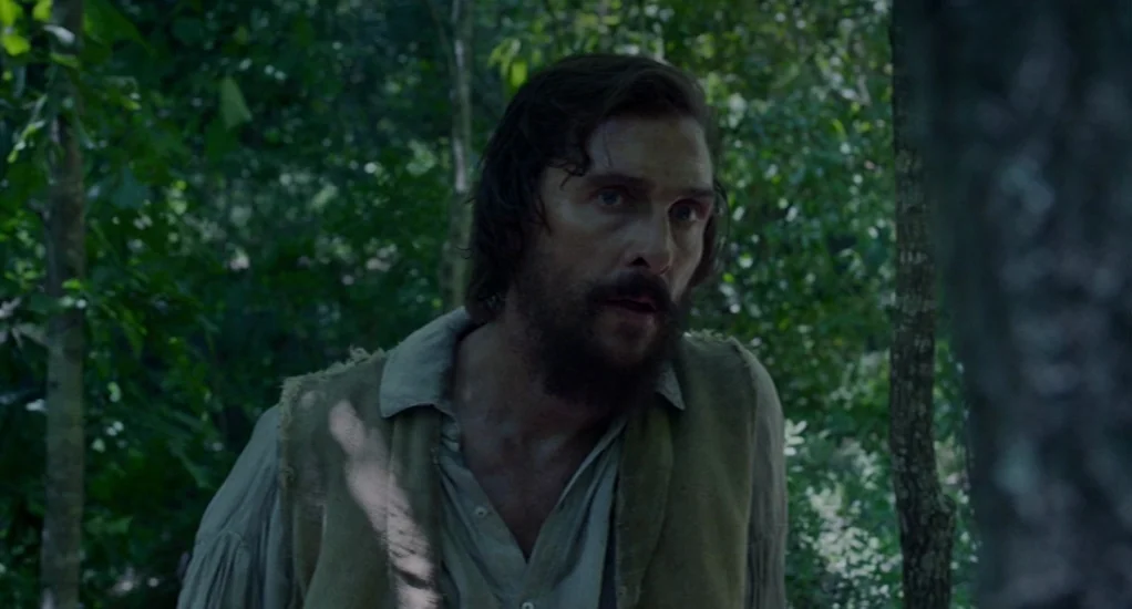 Free State of Jones (2016) movie still: medium — Dense, verdant woods surround a man standing between tree trunks in dappled sunlight. He gazes…