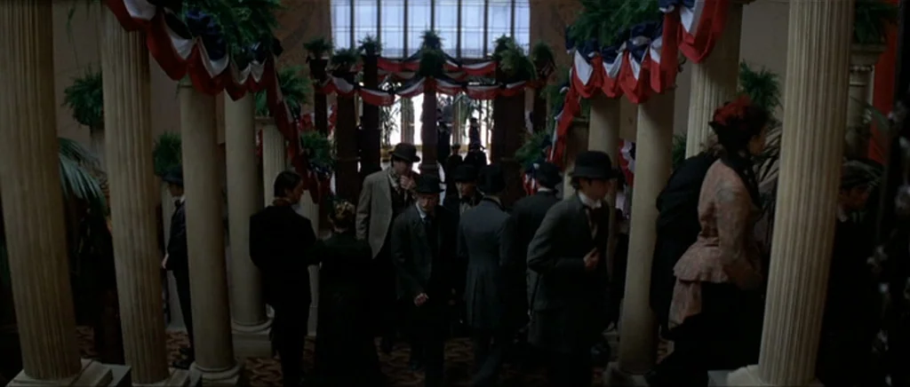 The Prestige (2006) movie still: wide — An 1800s ballroom features tall classical columns and patriotic red, white, and blue bunting. People dressed…