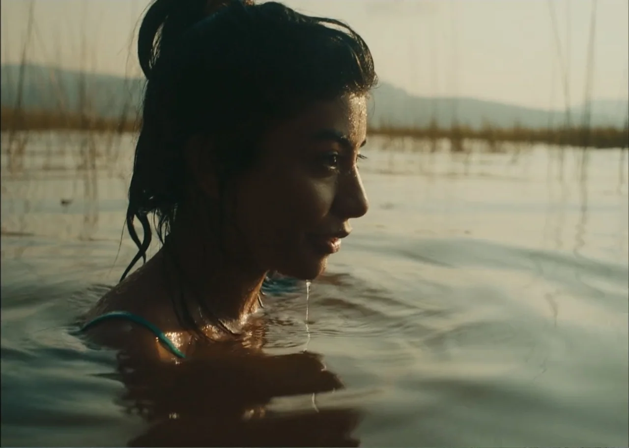 A Fisherman's Tale (1976) movie still: closeup — A woman stands in calm water during golden hour with reeds visible in distance. She is waist deep…